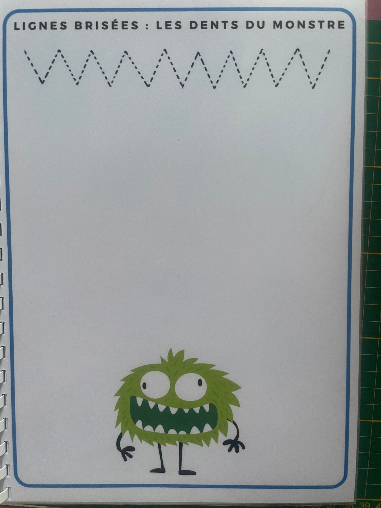 Page du livret de graphisme avec lignes brisées à tracer et dessin de monstre vert rigolo, support plastifié réutilisable A4.